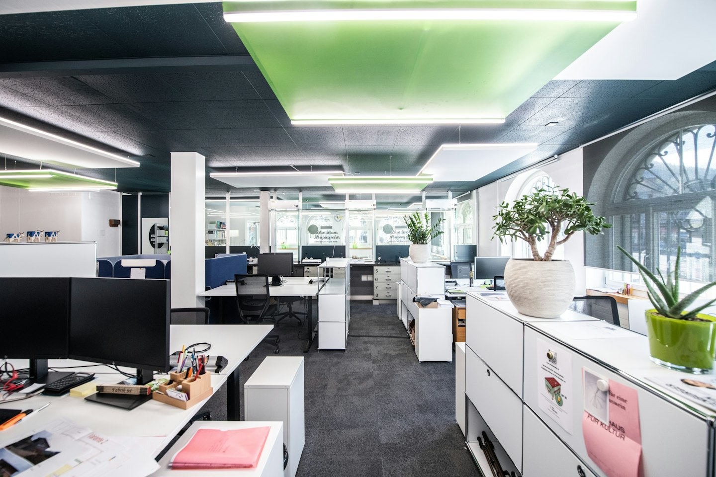Modern open-plan office with white workstations and large windows.
