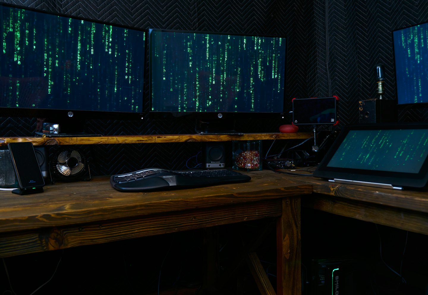 Multiple computer monitors displaying green code in a dark room.
